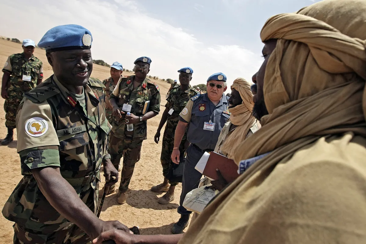 Peacekeeper and local man in traditional clothing shaking hands.