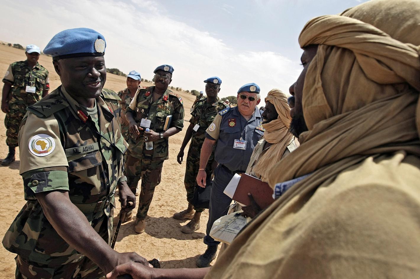 Peacekeeper and local man in traditional clothing shaking hands.